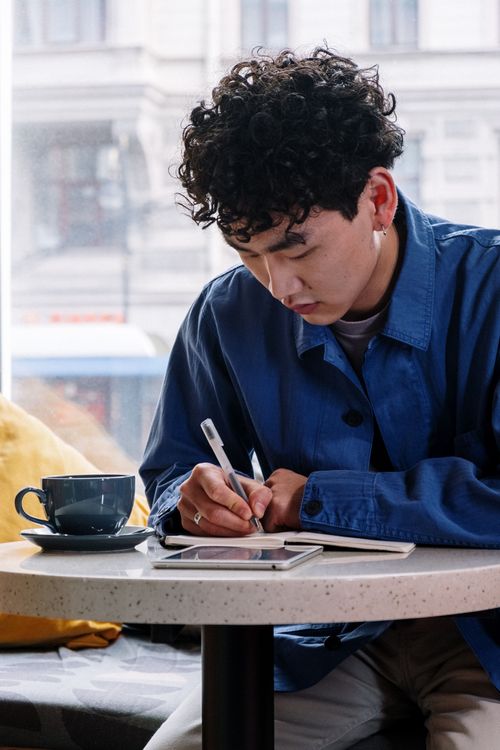 Homme concentré écrivant avec un café à proximité.